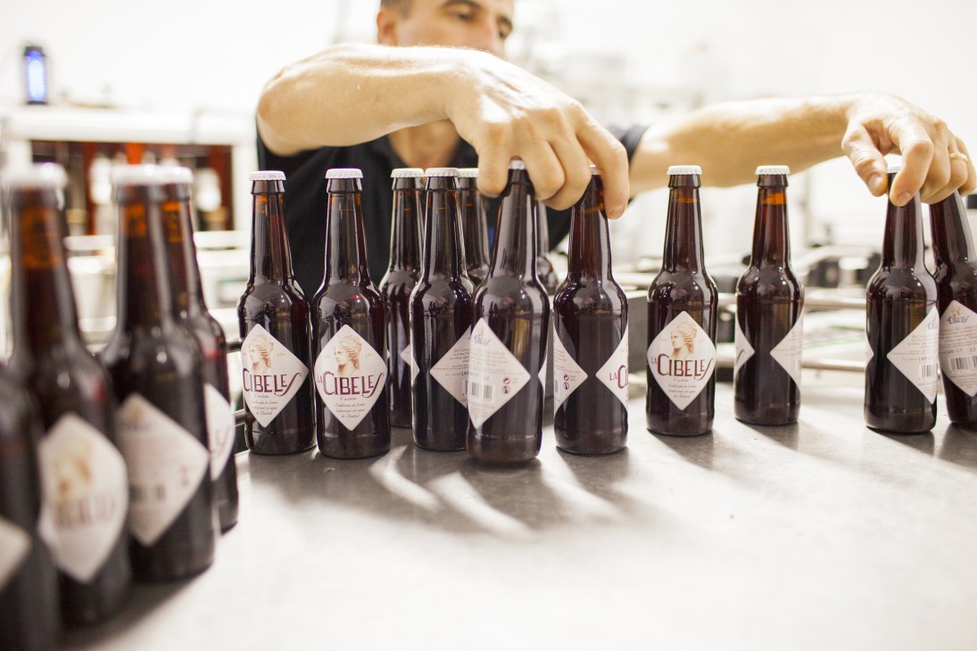 Hands arranging La Cibeles beer bottles with diamond-shaped labels on a table.