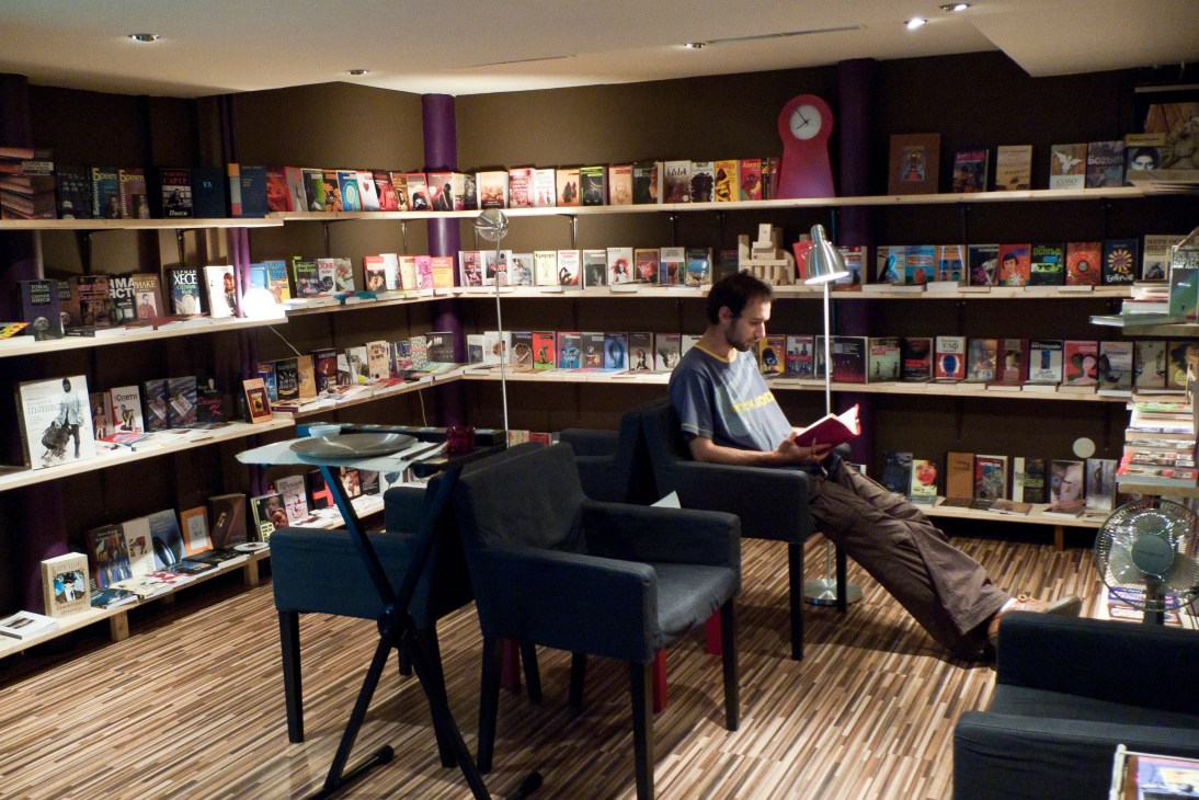 Man reading a book in PaperCake bookstore and chocolaterie with shelves of books lining curved walls.