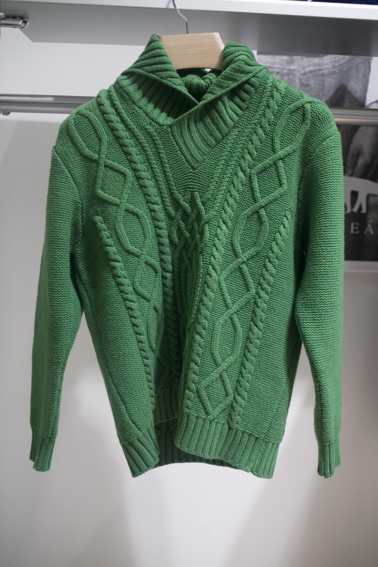Green cable-knit hooded sweater displayed on wooden hanger at Inis Meáin stand.