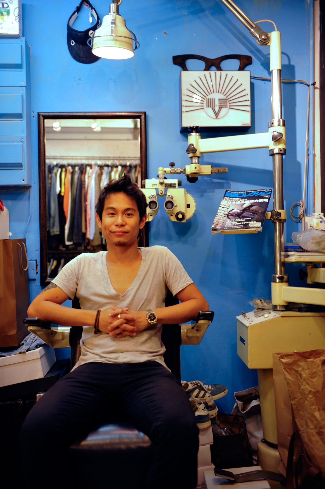 Thomas Lee sits in his vintage clothing shop Select 18, surrounded by retro eyewear and bright blue walls.