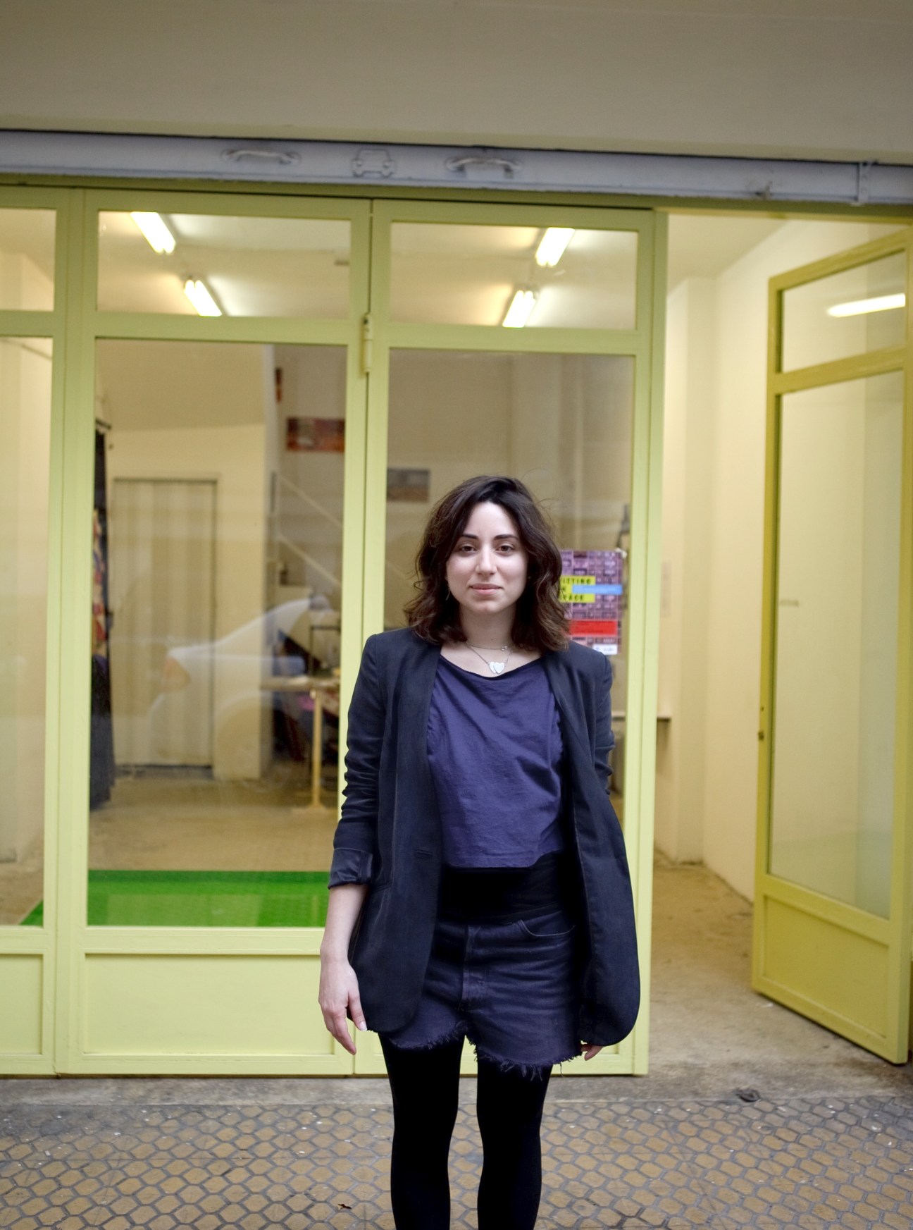 Woman standing in front of a storefront with yellow-green framed windows and doors.
