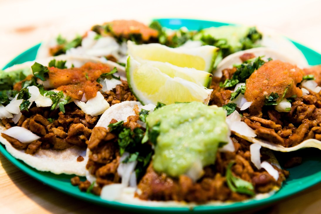 Mexican tacos al pastor served on a turquoise plate with lime wedges, onions, and cilantro.