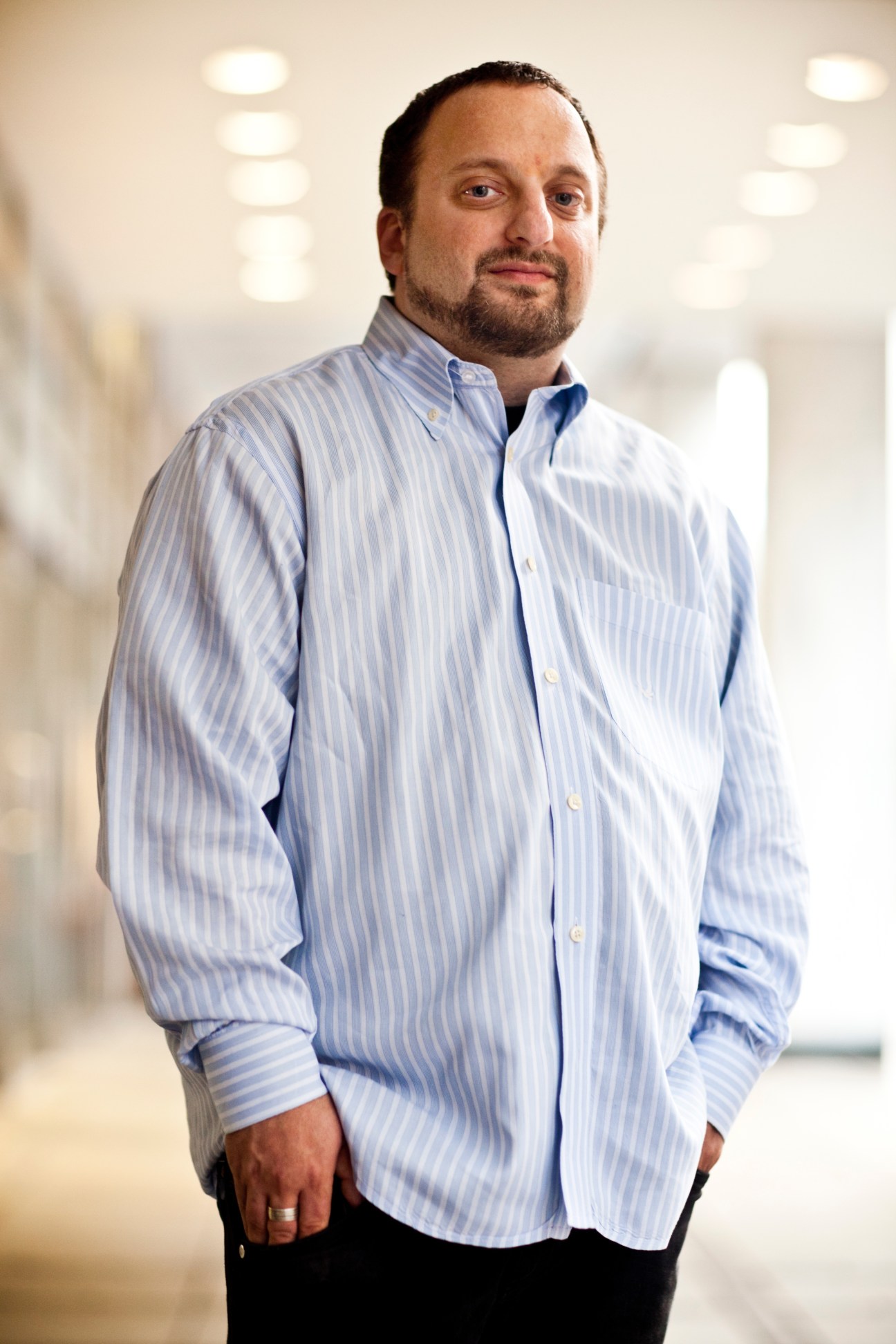 Scott Goodstein, political consultant, stands in a modern office hallway wearing a light blue striped shirt.