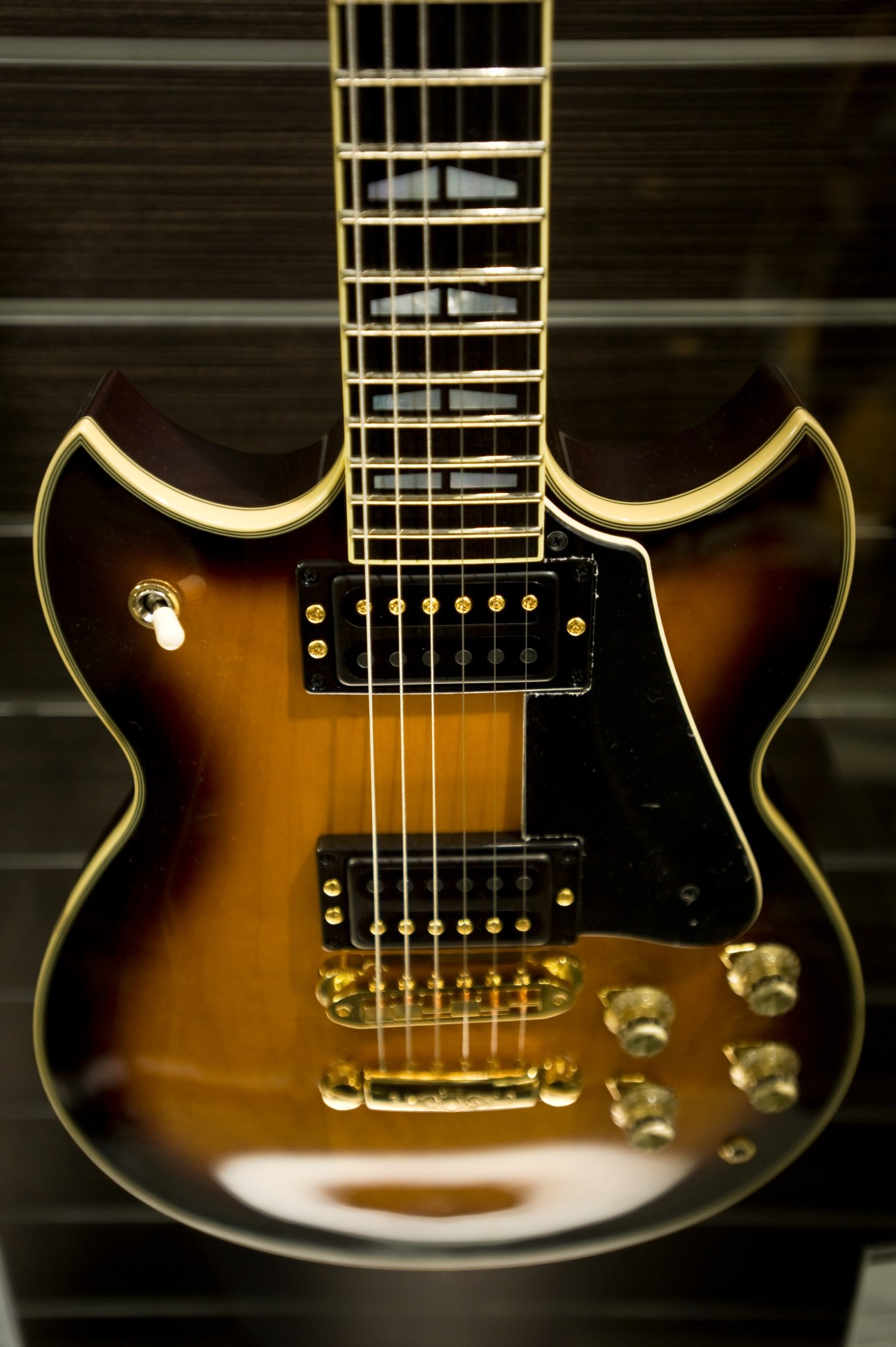 Semi-hollow body electric guitar with sunburst finish and gold hardware displayed against dark background.