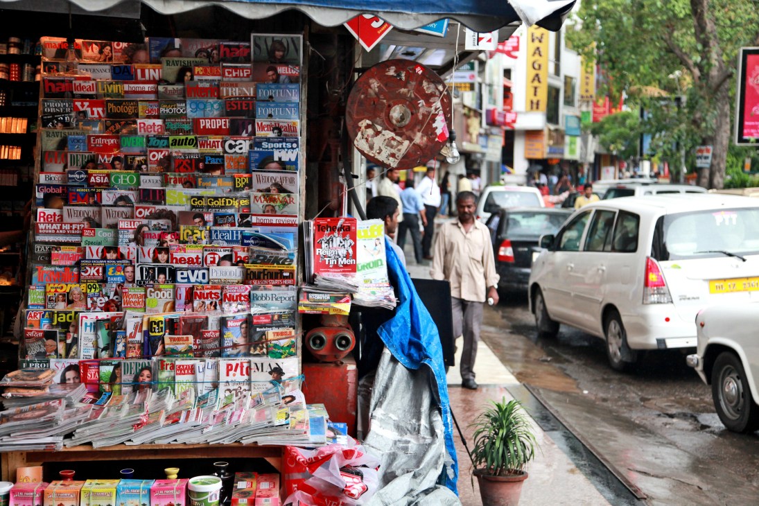 A New Delhi newsstand displaying colorful magazines and publications on a busy street.