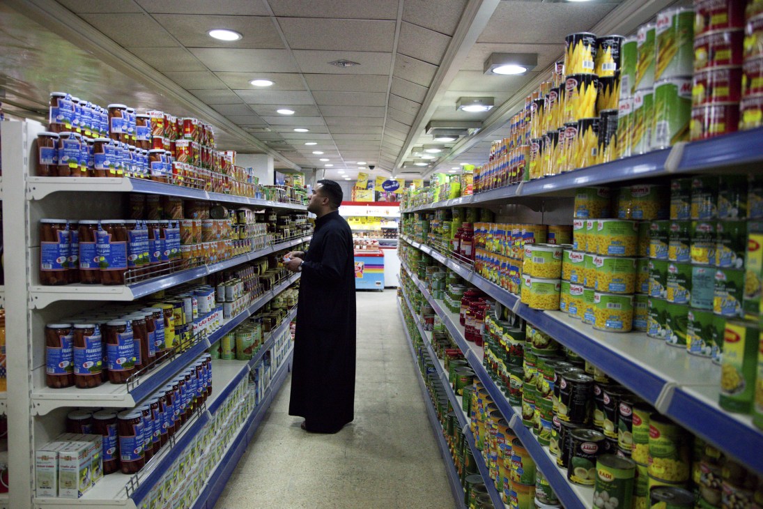 A man in dark clothing browses shelves stocked with colorful packaged goods in a supermarket aisle.