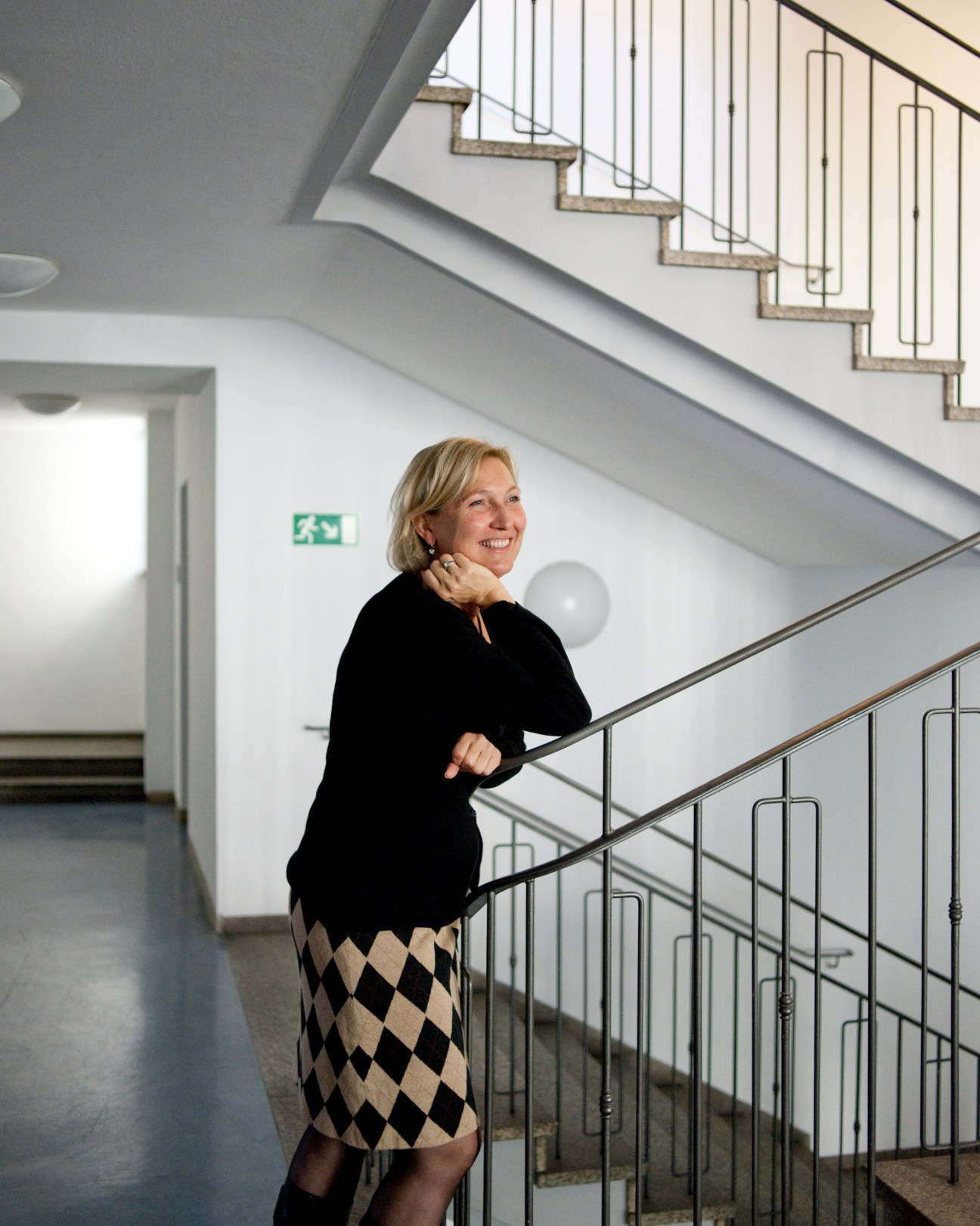 Katharina Knäusl smiles while standing on a staircase in a modern building with metal railings.