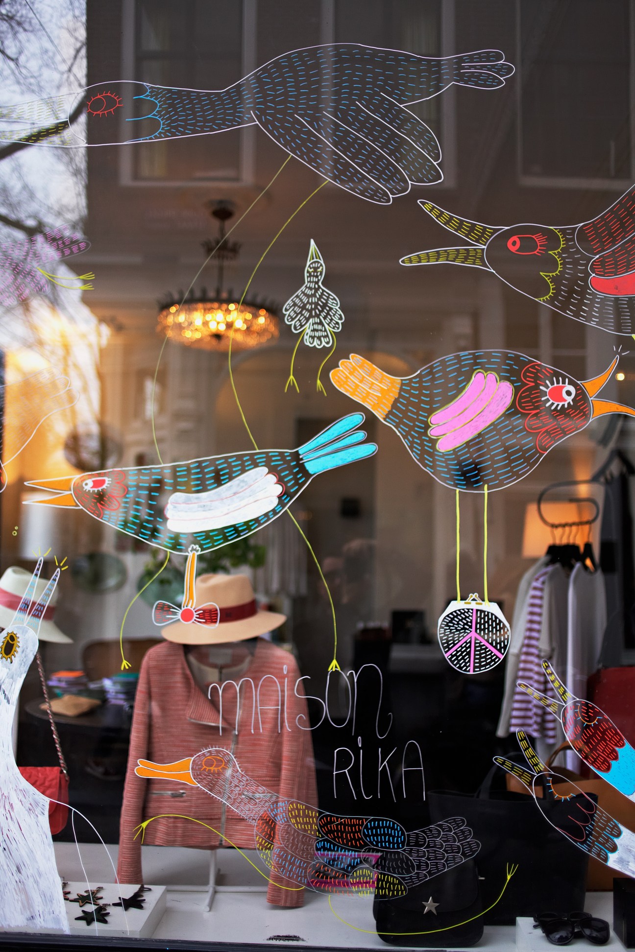 Whimsical window display at Maison Rika guesthouse featuring colorful illustrated birds and botanical designs on glass.
