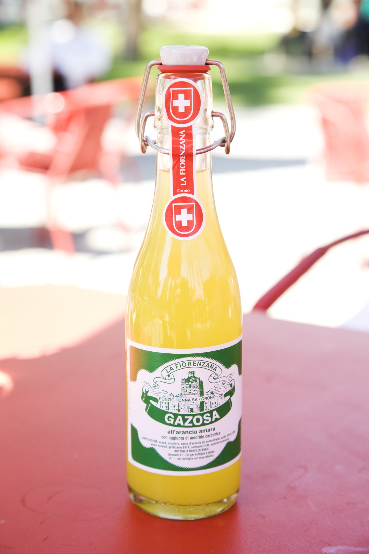 A bottle of La Fiorenzana Gazosa Italian lemonade with a flip-top closure sitting on a red surface outdoors.