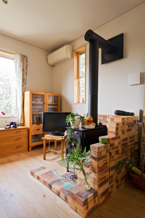 Interior of a residential unit at Yuimarl Nasu showing a wood-burning stove with black pipe, wooden furniture, and natural light from a window.