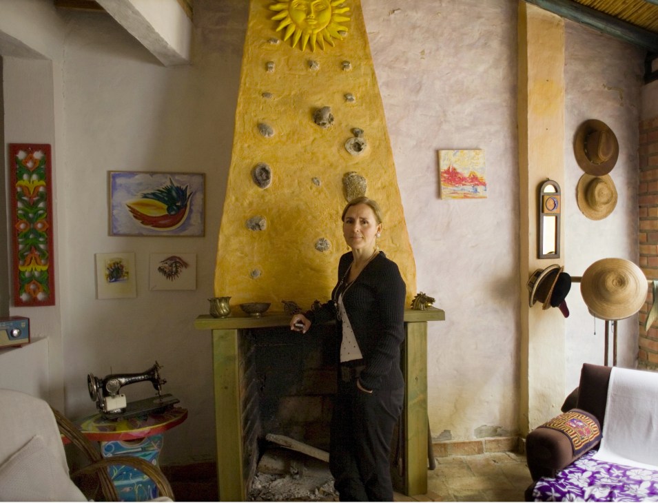 Designer Luna Diaz Sosa stands in a colorful interior with a bright yellow fireplace and folk art decorations.