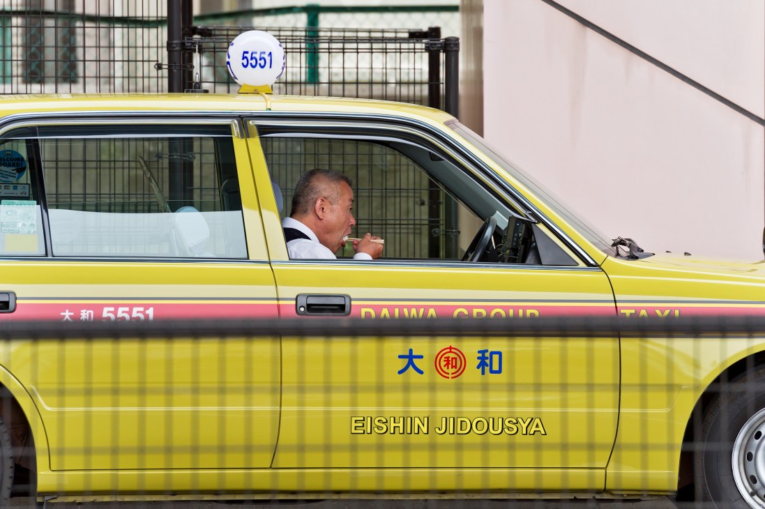 Tokyo taxi driver eating a bento box during break with meter off in yellow Daiwa taxi.