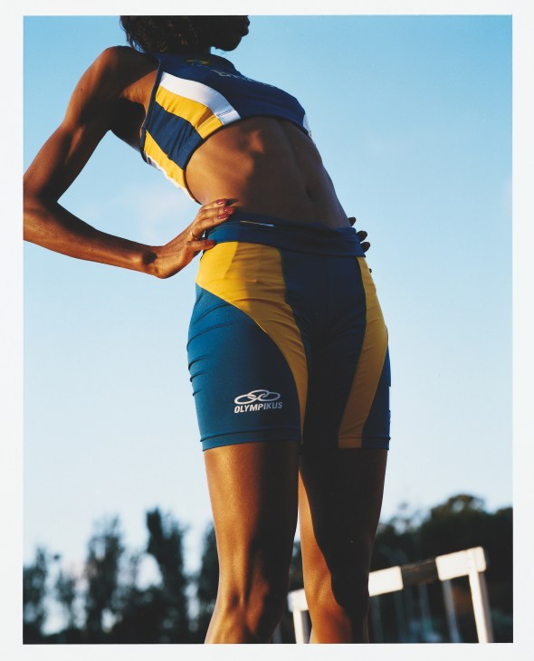 Brazilian athlete in blue and yellow Olympikus track uniform stretches against clear sky