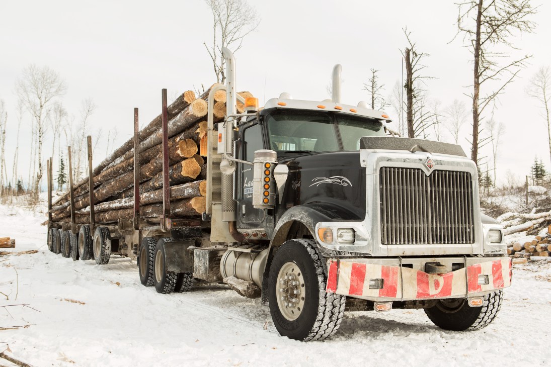 A logging truck loaded with timber in a snowy forest clearing in winter.