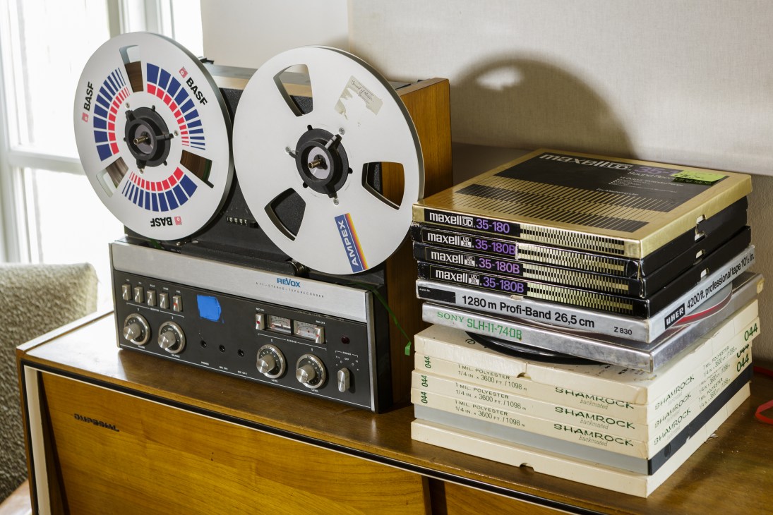 Vintage reel-to-reel tape recorder with BASF reels on a wooden surface next to stacked audio cassettes and books.