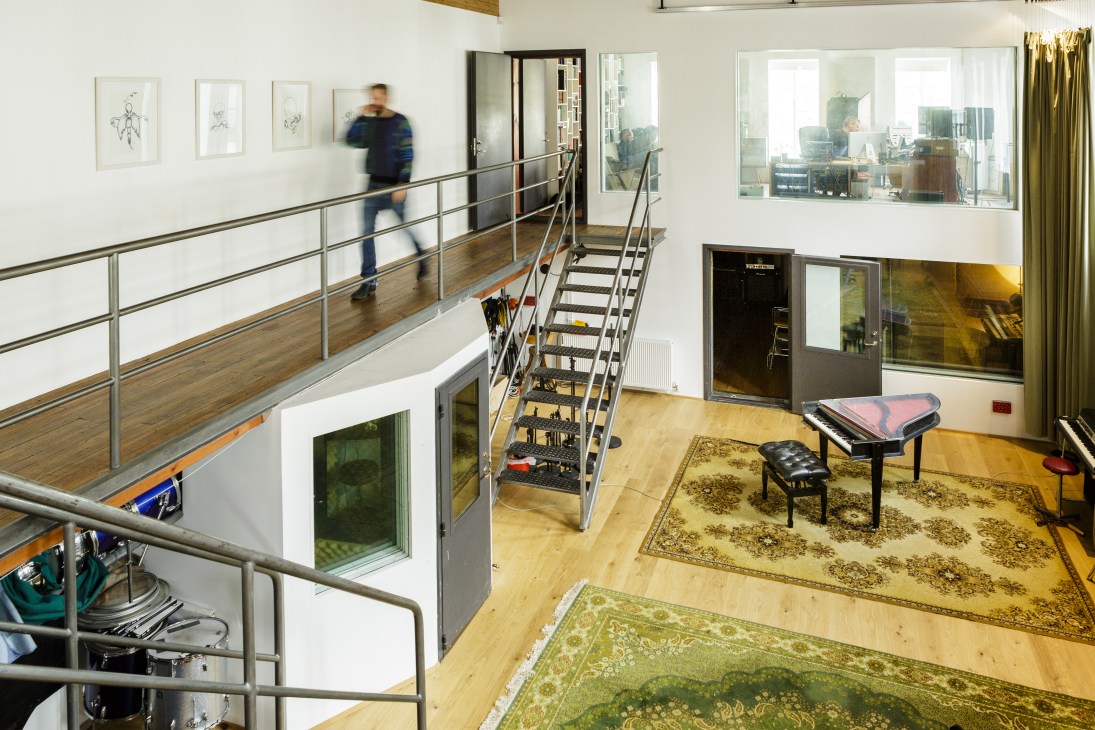 A modern studio vestibule with a mezzanine level overlooking an open floor space with wooden flooring and patterned rugs.