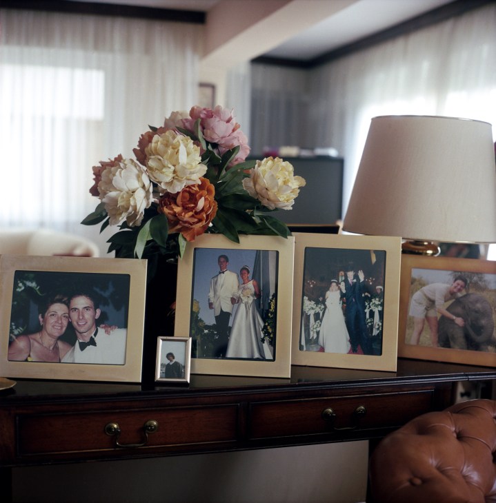 Family photographs in frames displayed on a wooden dresser with flowers and a lamp.
