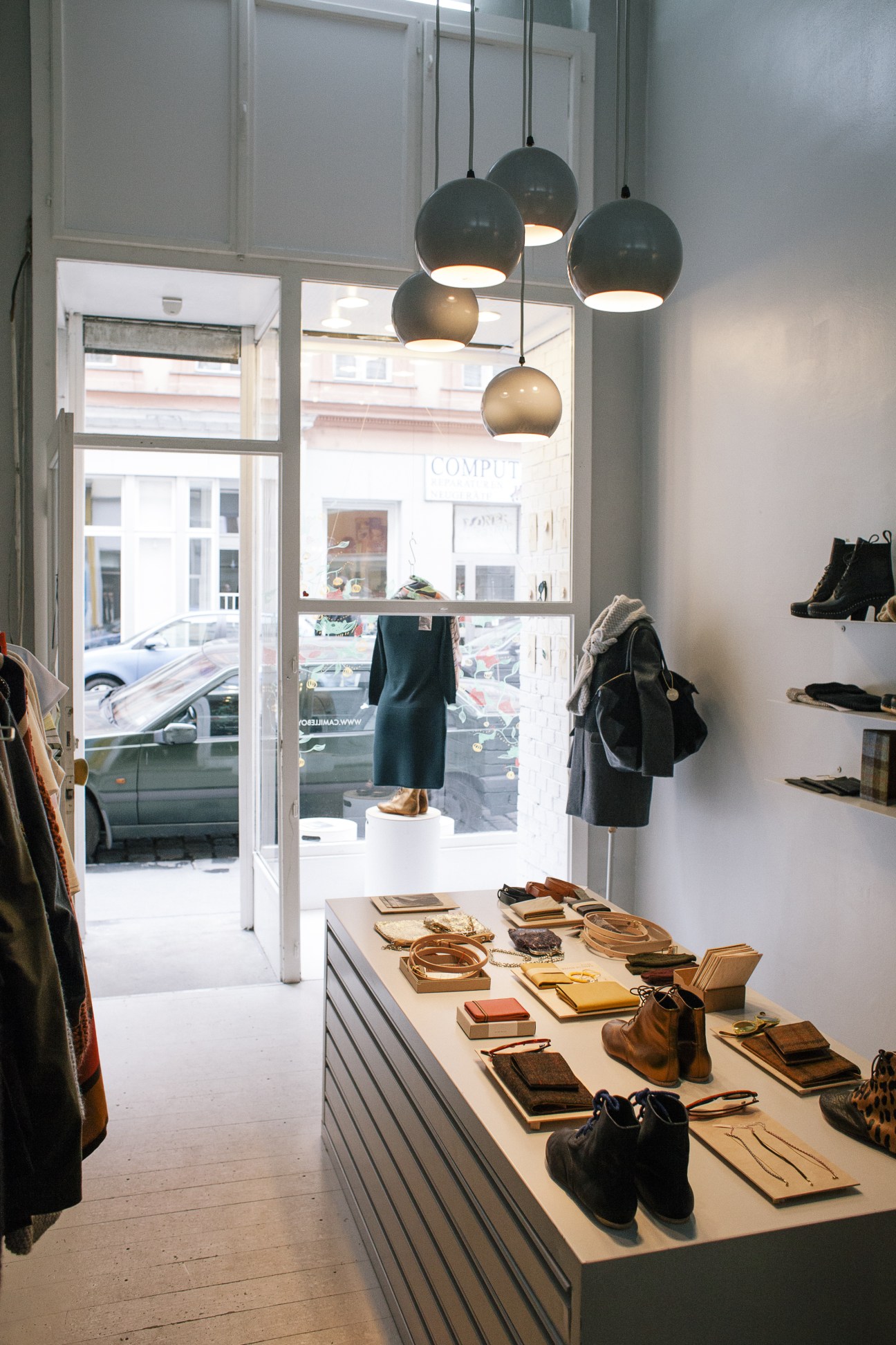 Interior of Camille Boyer fashion boutique with leather accessories displayed on a central table and hanging pendant lights.