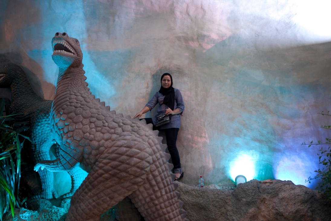 Woman in hijab posing next to a large sculpted dinosaur at Kish Dolphin Park