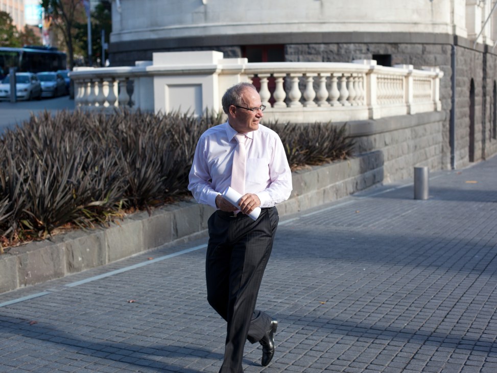 Man in light blue shirt and dark trousers jogging on a paved waterfront promenade.