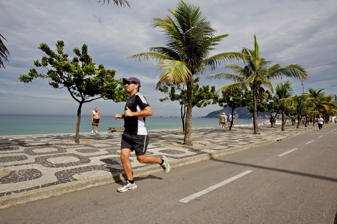 A jogger runs along a beachside promenade in Rio de Janeiro with palm trees and ocean views.