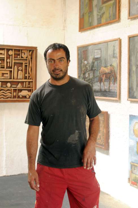 Richard San Martín, an artist and sculptor, standing in front of framed artworks in his studio.