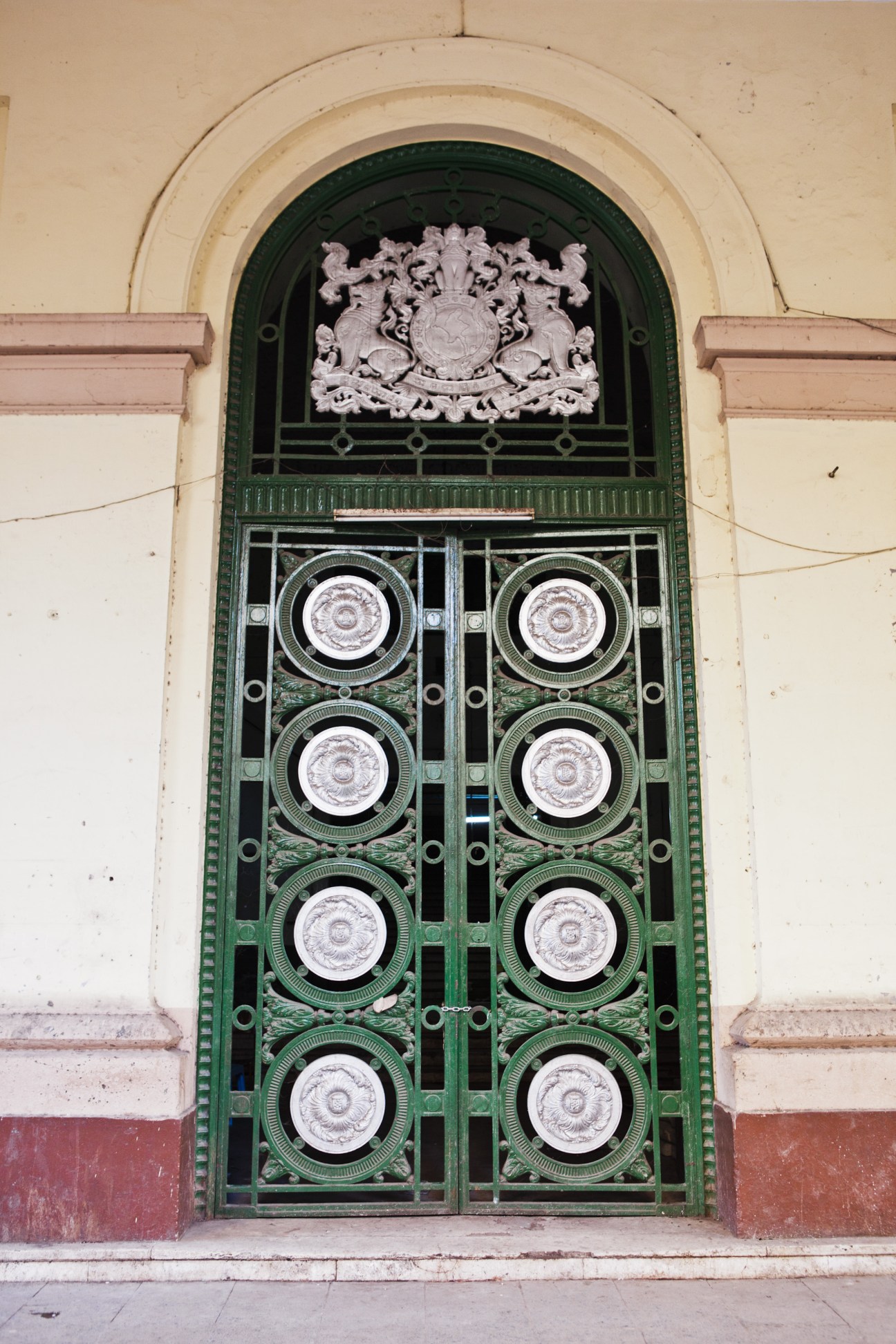 Ornate green colonial door with white porcelain medallions and British coat of arms crest.