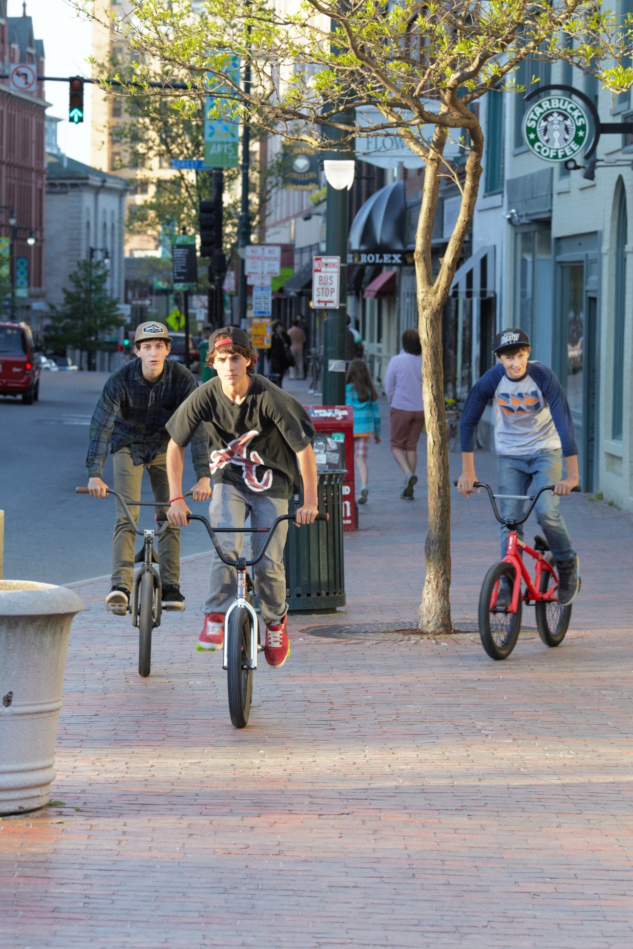 Three cyclists riding on a brick pedestrian street lined with shops and trees in Portland