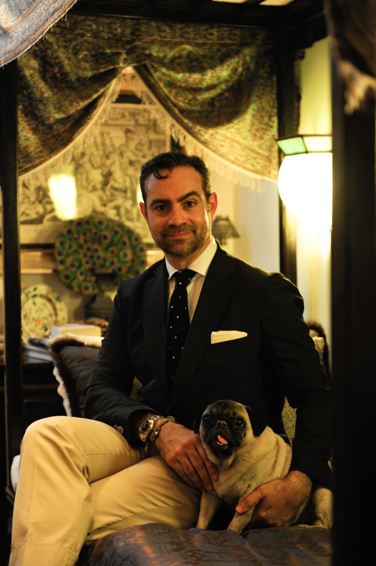 Olivier de Molina in a black suit sitting indoors with his pug dog Wallis