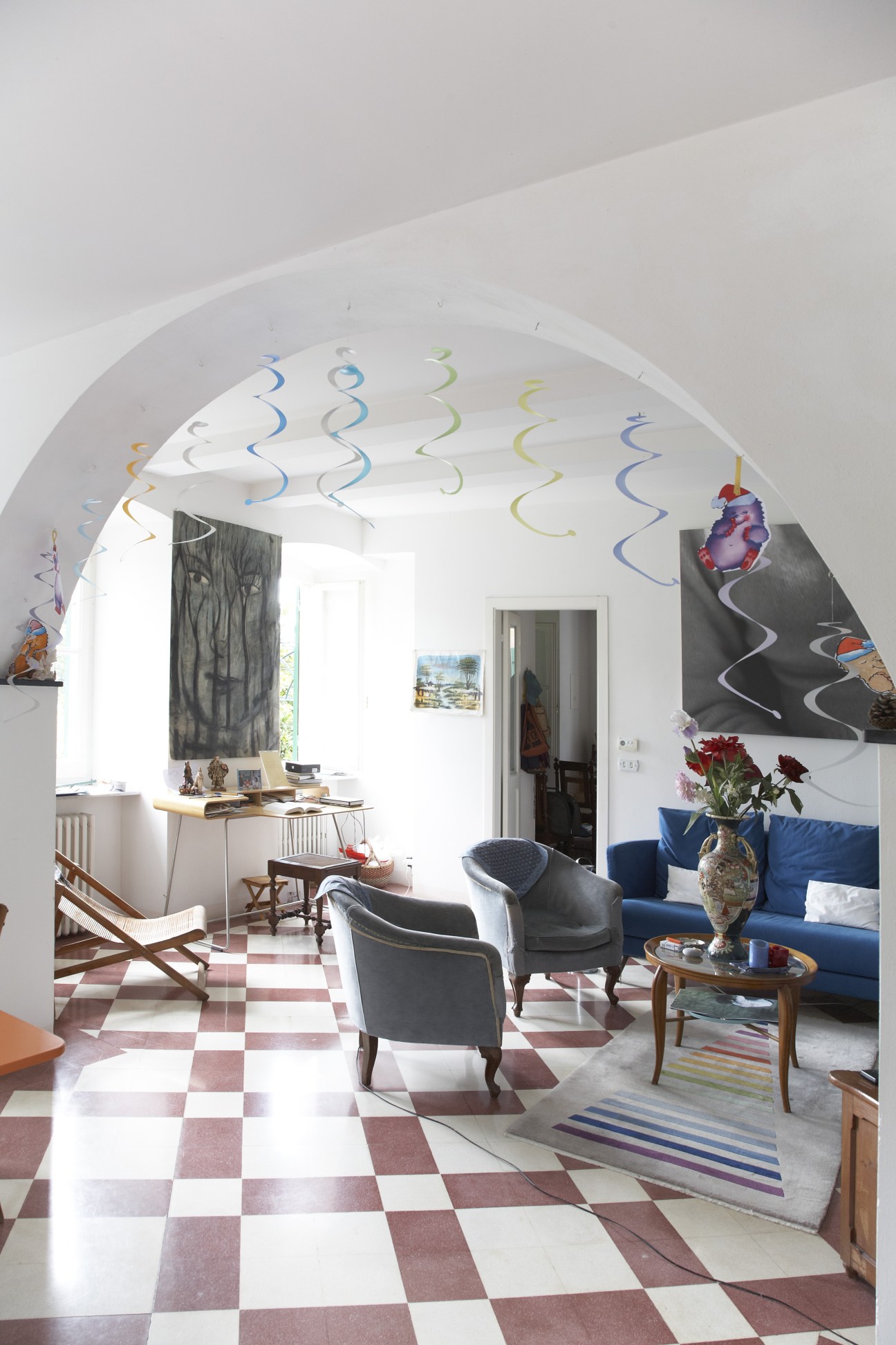 Bright modernist interior with arched ceiling, checkered floor, blue sofa, and colorful spiral decorations.