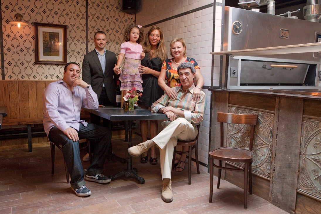 Family members pose together in Rubirosa restaurant's vintage-style interior with exposed brick and wood furnishings.