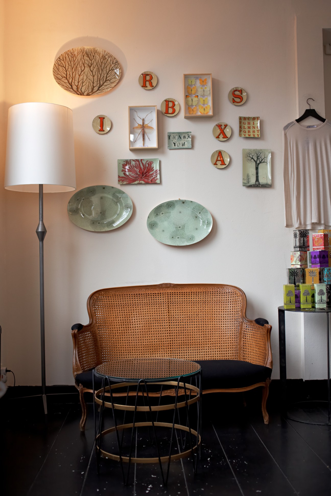 Interior of Maison Rika boutique with rattan chair, wall-mounted decorative items, and clothing displayed on right side.