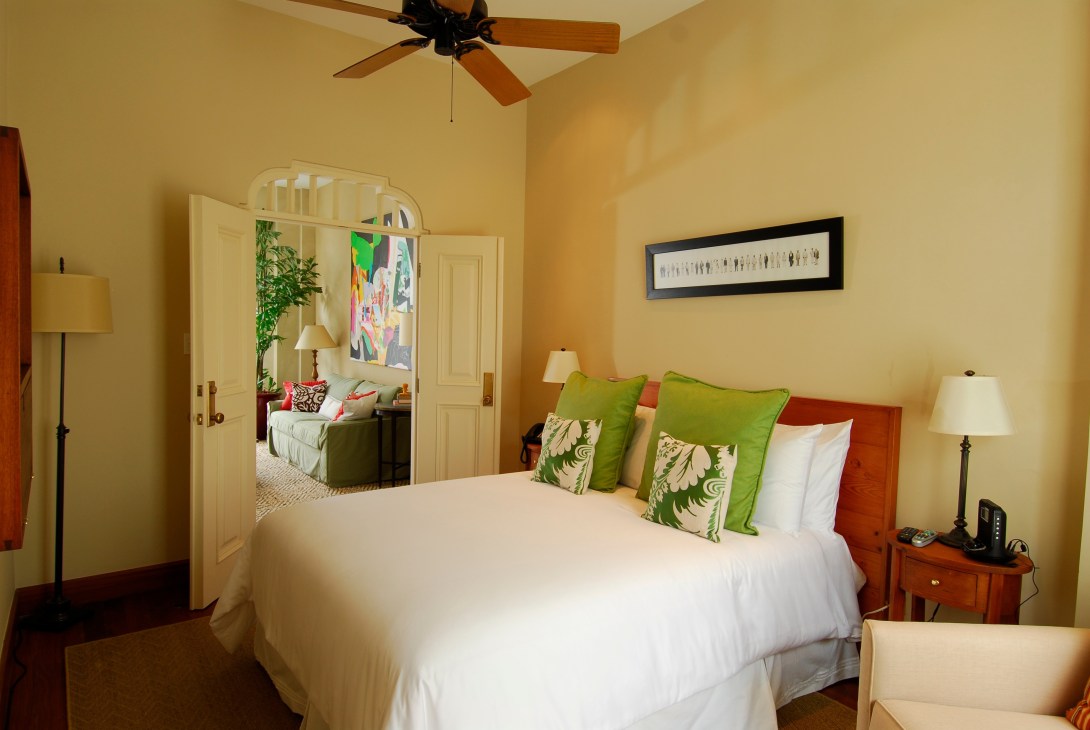 Bright hotel bedroom with yellow walls, white bed with green pillows, and wood furniture at Las Clementinas Panama City.