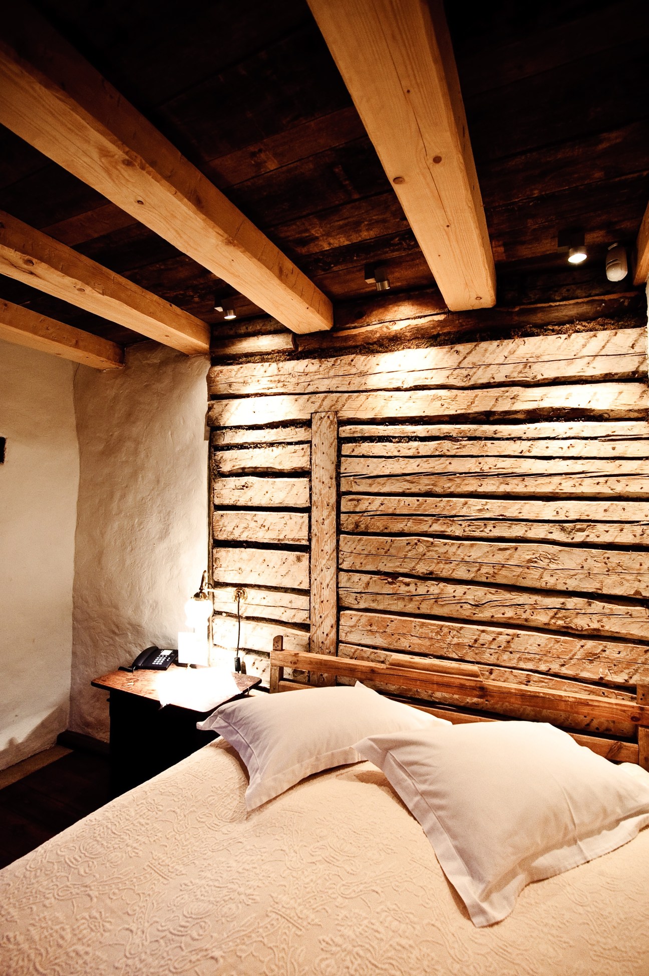 Rustic bedroom with exposed wooden beams, log walls, and a bed with white pillows at Pädaste Manor.