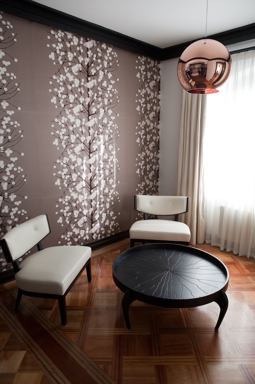 Modern hotel interior with floral wallpaper, white chairs, black table, and copper pendant light.