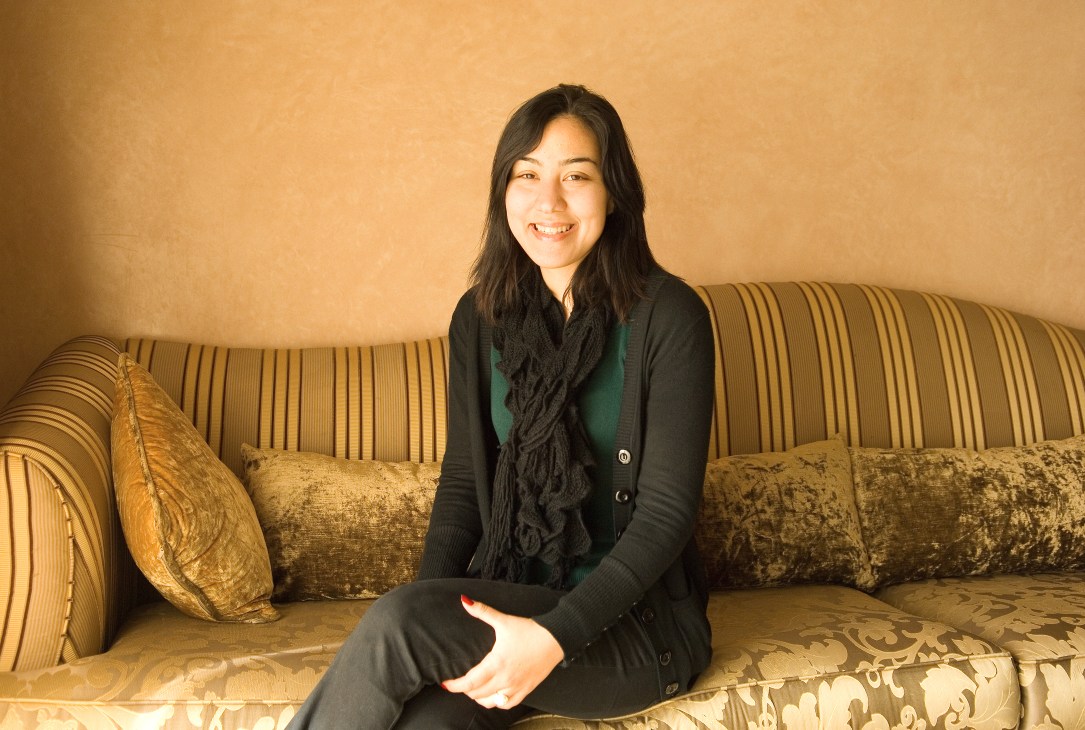 Sana Khatib, a 29-year-old estate agent, sits on a striped gold sofa wearing a black cardigan and scarf.
