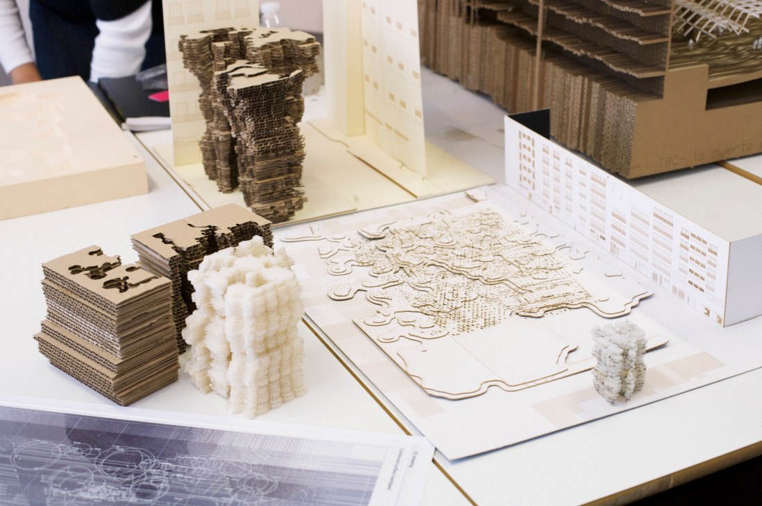 Architecture student's work-in-progress models and drawings displayed on a white desk.