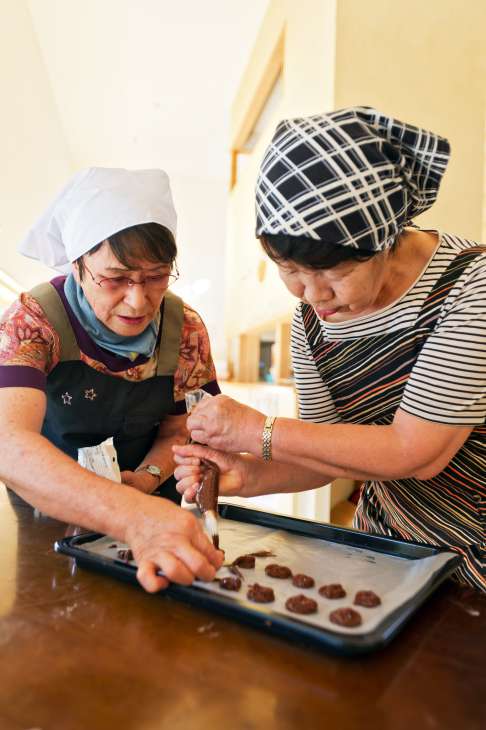 Two elderly women preparing chocolate treats on a baking tray at Yuimarl Nasu in Japan.