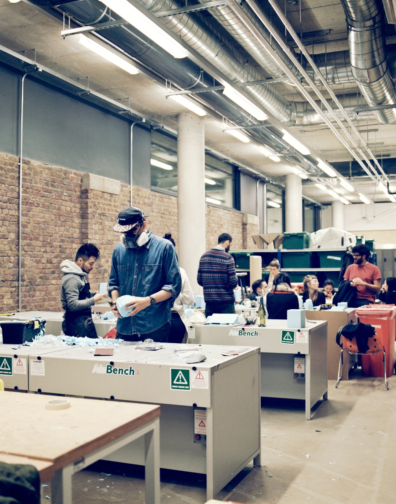Students work at benches in a bright workshop space with exposed brick and industrial ceiling.