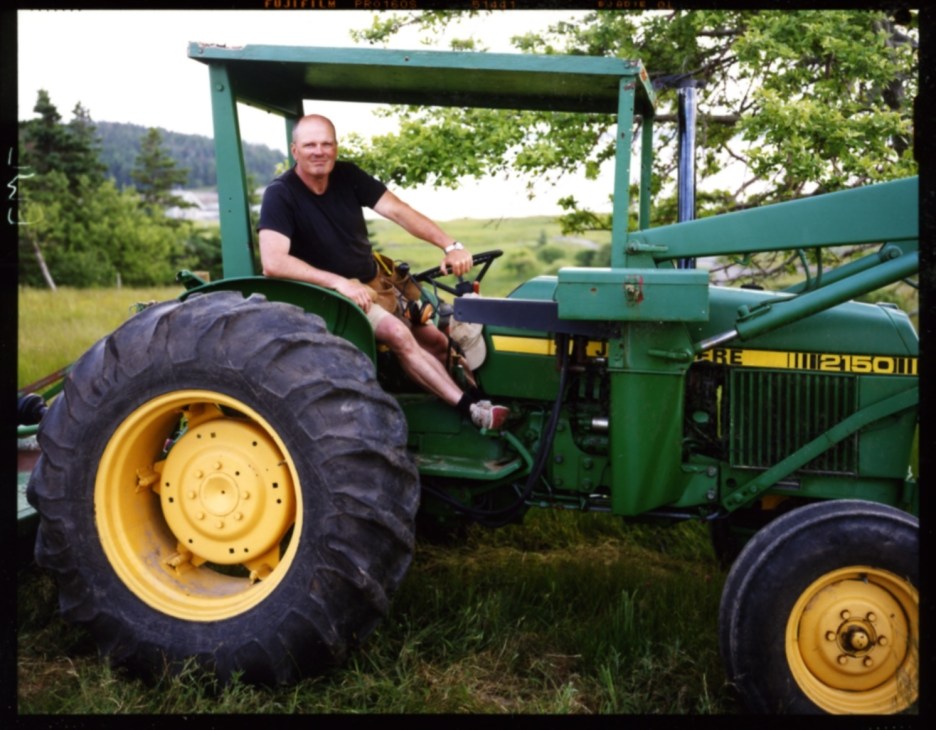 Brian MacKay-Lyons sits on a green tractor with large yellow wheels in a rural landscape.