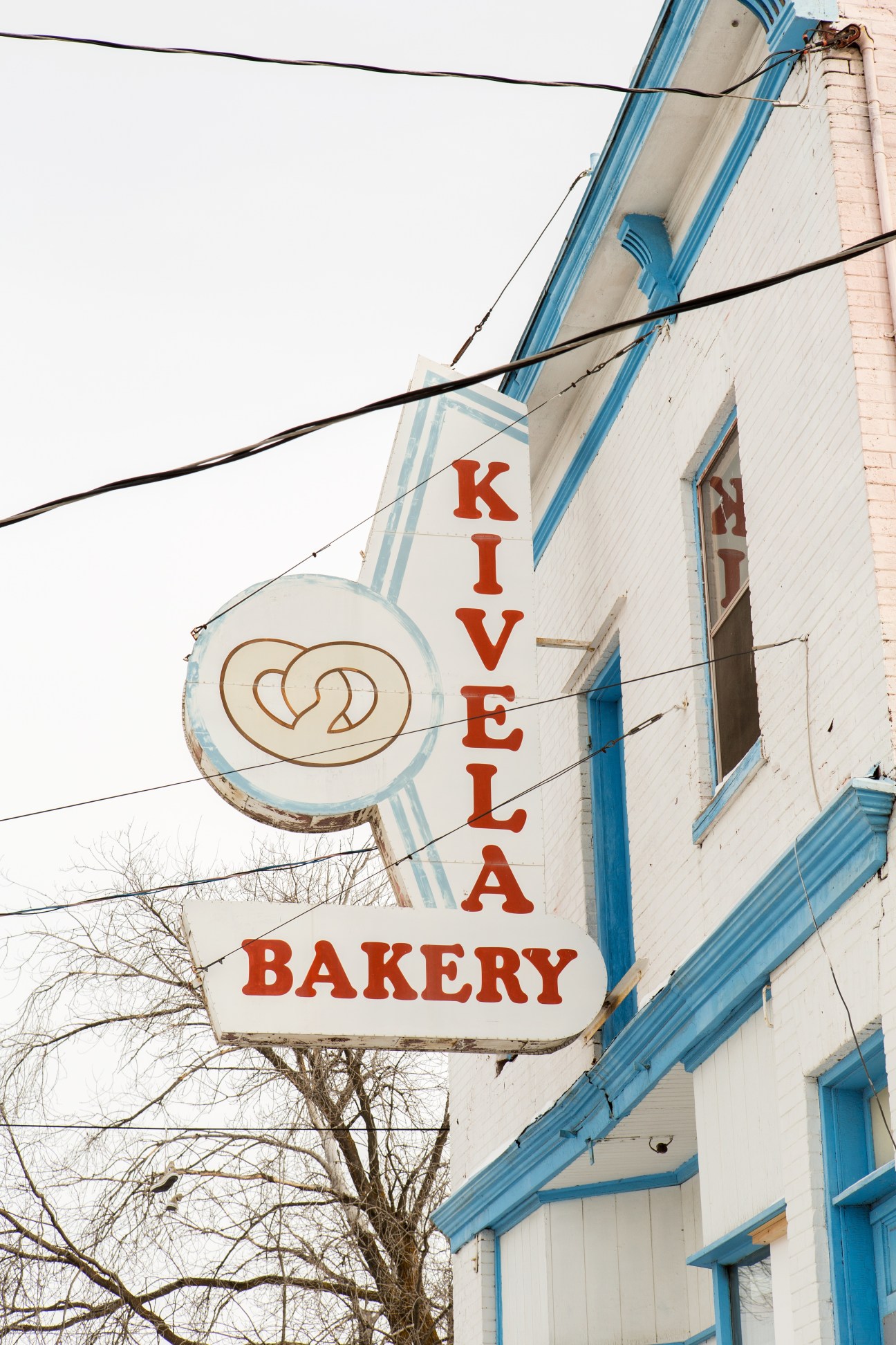 Kivela Bakery sign with red lettering and pretzels logo on white building with blue trim.
