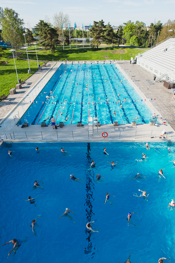 Aerial view of Helsinki Swimming Stadium with two pools filled with swimmers and green lawns surrounding the facility.