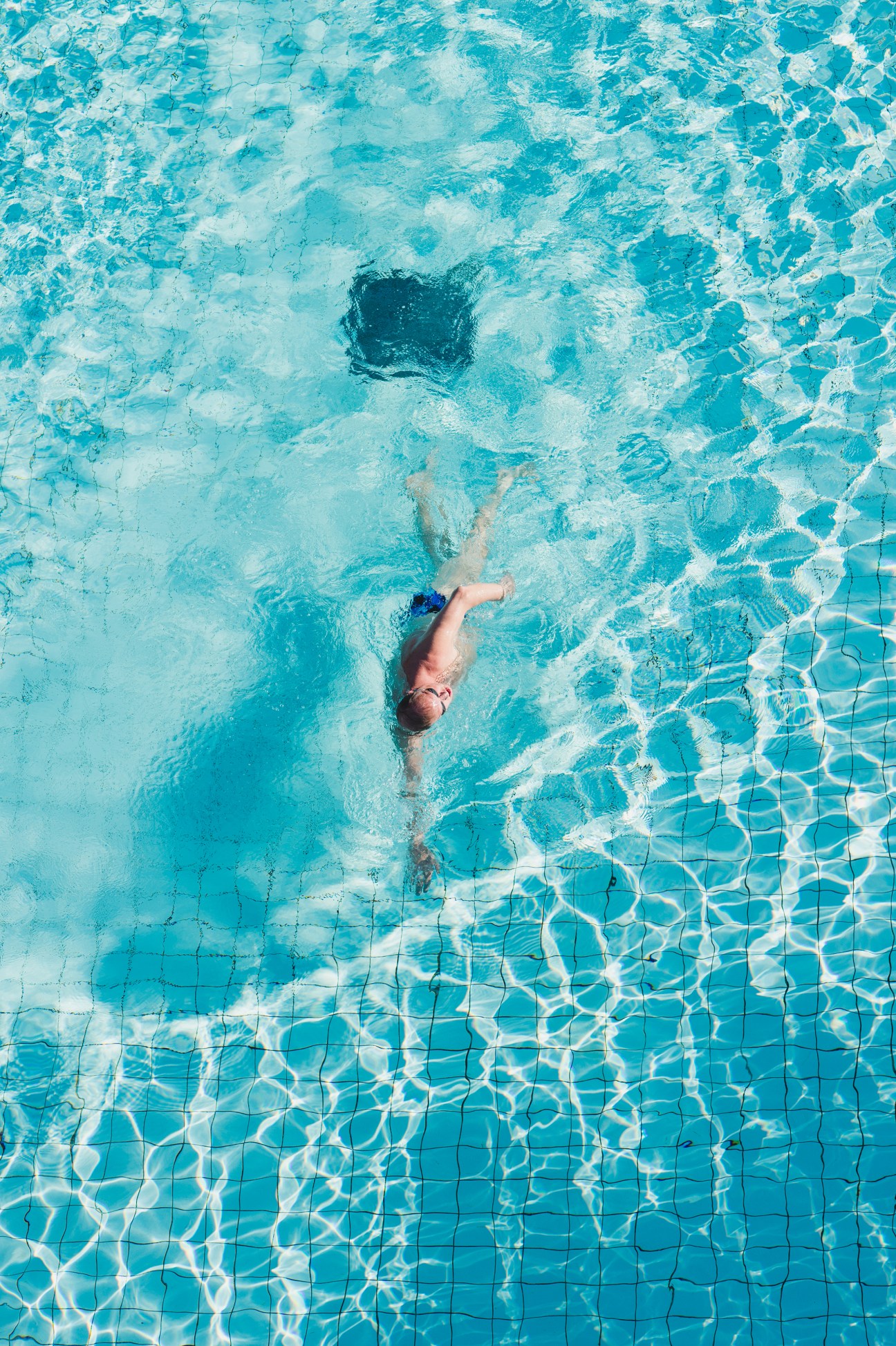 Swimmer doing freestyle stroke in a clear turquoise pool with visible lane divider.