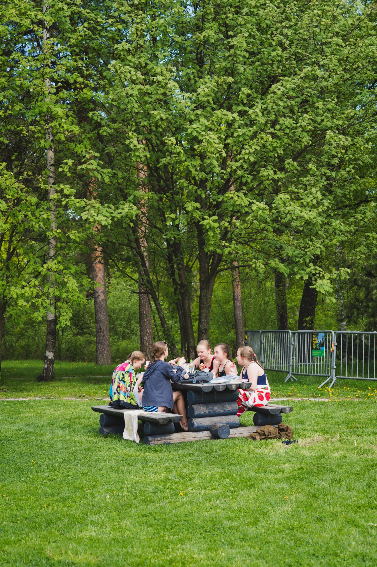 A group of swimmers enjoy a picnic at a table in a leafy park surrounding Helsinki Swimming Stadium.