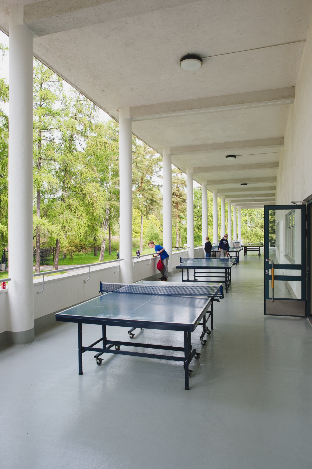 Table tennis tables in a covered pavilion at Helsinki Swimming Stadium with forest views.