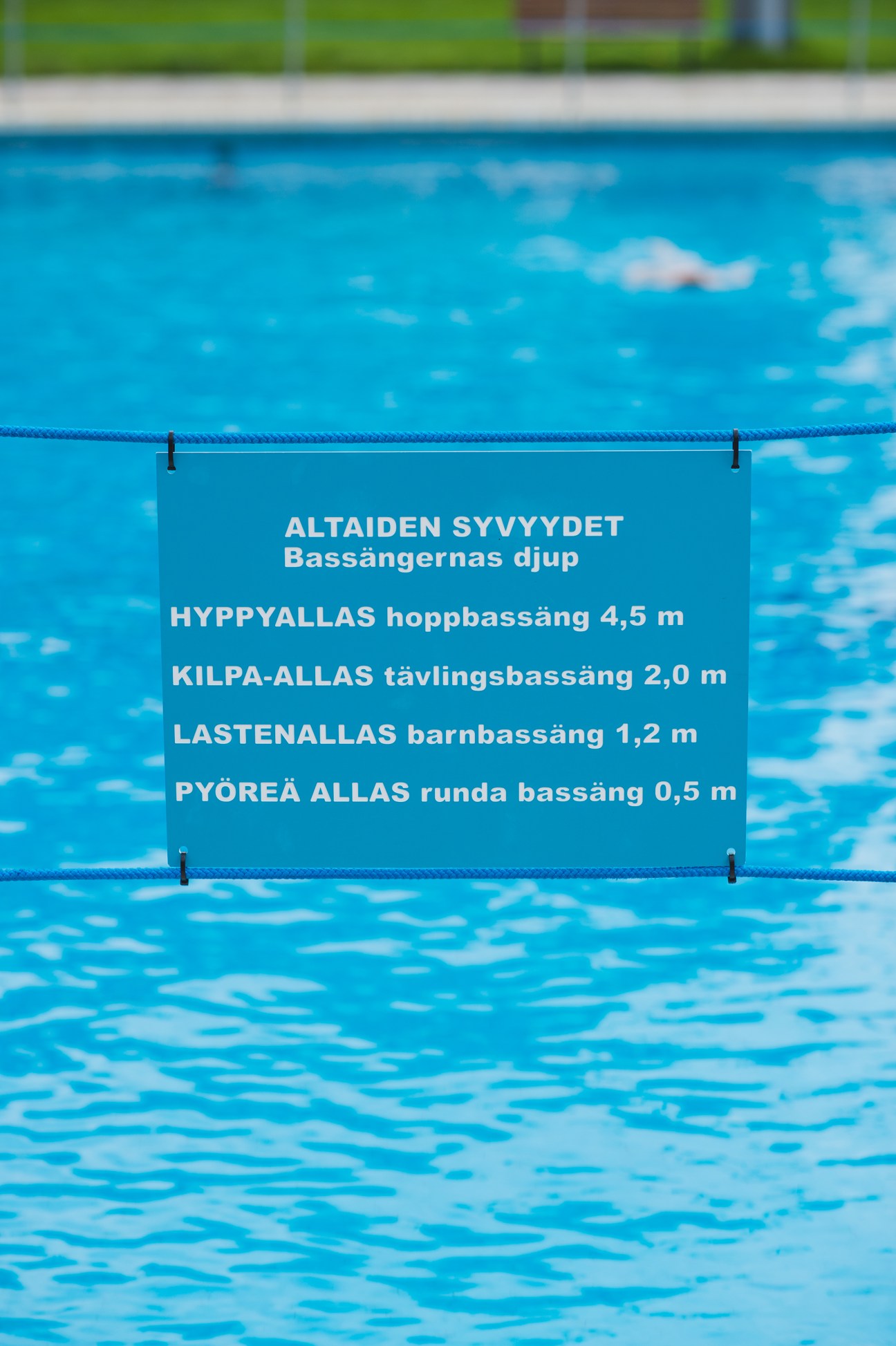 Blue swimming pool with an informational sign in Finnish listing four pools at varying depths.