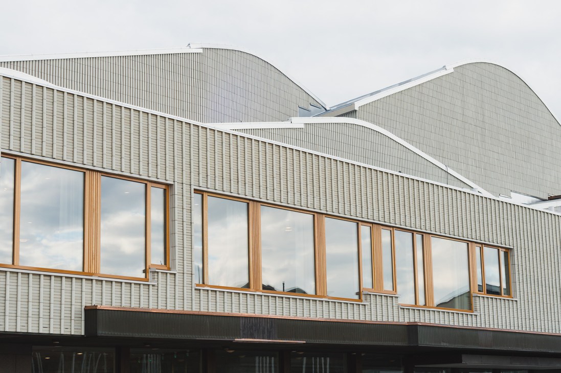 Lappia Hall's distinctive undulating metal roof with curved white trim and large wooden-framed windows reflecting the sky.