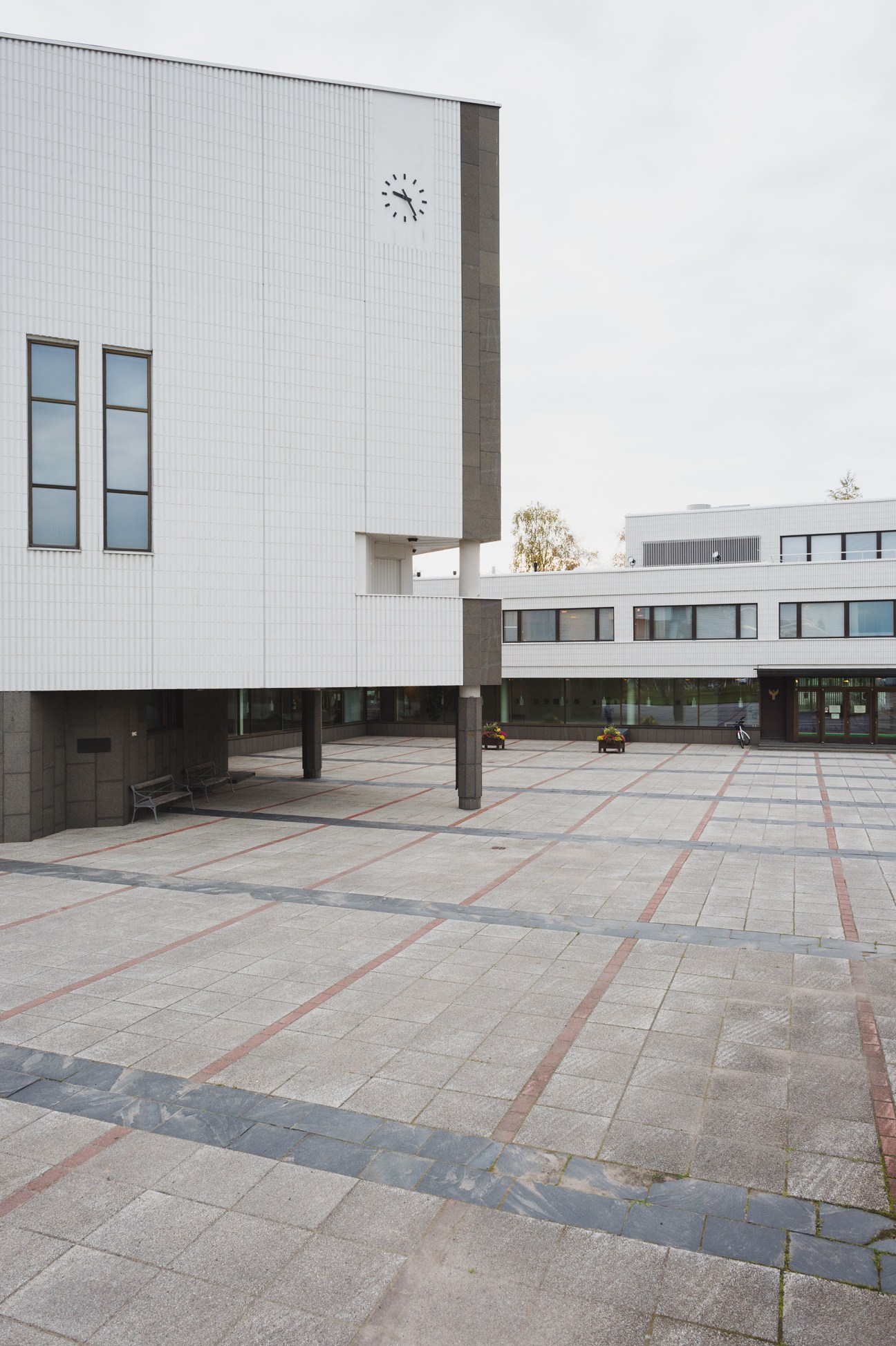 Modernist white city hall building with clock on facade overlooking paved plaza