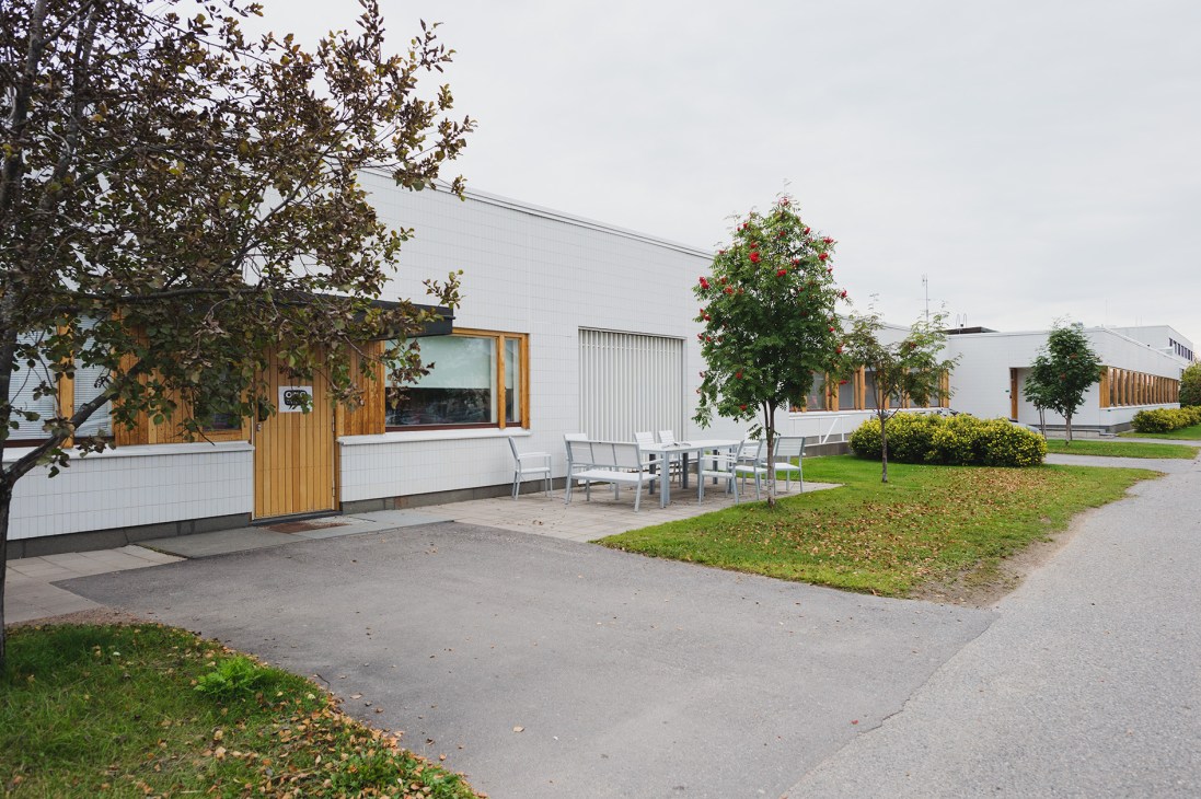 Modernist building exterior with white walls, wooden accents and large windows surrounded by landscaped gardens.