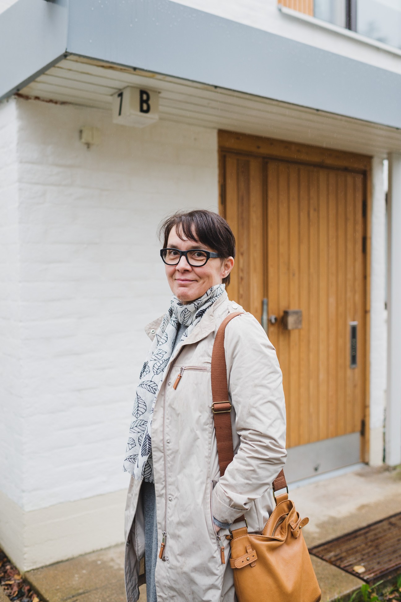 Woman standing outside a modernist residential building with white walls and wooden door in Rovaniemi.